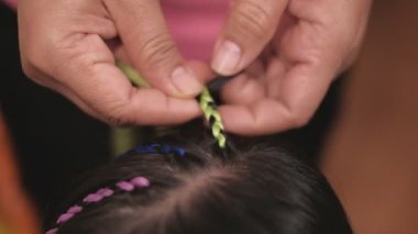 Yakın plan VDO: Güzel, uzun siyah saçlı Asyalı kız güzellik salonunda çok renkli ipliklerle örülüyor. Çocuk modası, örgü ören örgü ören örgü ören yün örgüler..