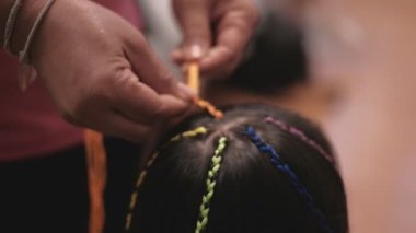Yakın plan VDO: Güzel, uzun siyah saçlı Asyalı kız güzellik salonunda çok renkli ipliklerle örülüyor. Çocuk modası, örgü ören örgü ören örgü ören yün örgüler..