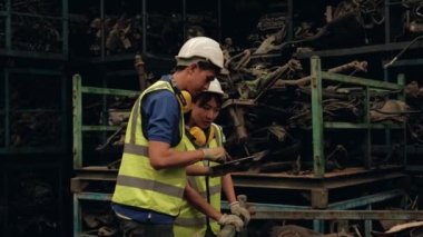 Üniformalı ve kasklı Asyalı erkek ve kadın işçiler, yedek araba deposu fabrikasının personel stok kontrolü. Eski motorları ve otomotiv endüstrisi siparişlerini kontrol etmek için tablet kullanmak.