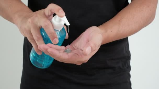 白色背景的中景镜头 一名身穿黑色T恤的男子正在用瓶子中的酒精凝胶清洁双手和手指 以防止细菌感染 科沃德19型和健康的卫生状况 — 图库视频影像