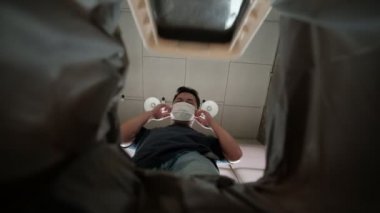Düşük açı. Adam kullanılmış maskesini çöp kutusuna atıyor. Koronavirüsün (COVID-19) ve diğer hastalıkların yayılmasına yol açabileceği için, tehlikeli ve sağlığını kısıtlıyor..