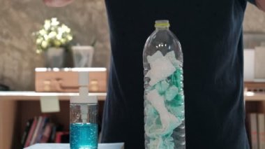 Adam kullanılmış maskeyi boş bir şişeye koyar ve ellerini hijyen için alkol jeliyle temizler, böylece hastalığın yayılmasını, koronavirüsün enfeksiyonunu (COVID-19) ve ofisteki bakterileri önler..