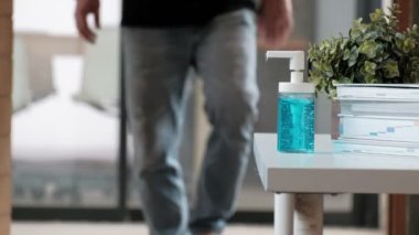Yakın çekim: Sıradan bir adam, sağlık hijyeni için bir şişe alkol jeli, el dezenfektanı ve Coronavirus (Covid-19) gibi hastalık ve bakterileri evde çalışırken önlemek için baskı yapıyor..