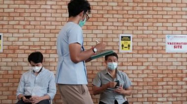 Hemşire, aşılanmış insan kuyruğunu kontrol eder, Coronavirus 'u (COVID-19) sağlık kampanyası için korur. Hastalar, hastalıktan korunmak için oturup, sosyal mesafeyi koruyorlar ve maske takıyorlar..