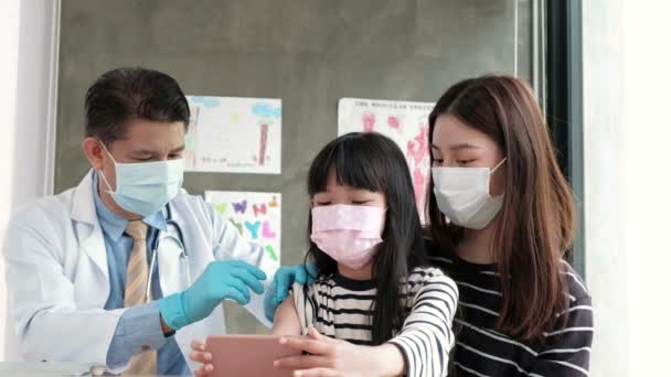 病院の診療所で医師が予防接種をしている間 母親と携帯電話で自撮りの肖像画を撮るアジアの少女 Covid 注射は熱や病気を薬で治療します — ストック動画