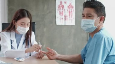Kadın doktor, erkek bir Asyalı hastanın kanını diyabet ve sağlık testleri için insülin ölçer cihazıyla hastane kliniğinde muayene ediyor. Glikoz kontrolü ve tıbbi tedavi için kullanılan laboratuvar analizi.