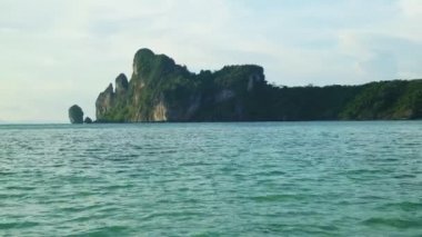 Pan tekniği VDO: Turkuaz deniz dalgaları ve Tayland kıyılarındaki yeşil kayalık uçurumlardan oluşan güzel bir manzara. Doğal olarak, turistler yaz tatilinde dinlenmeyi severler..