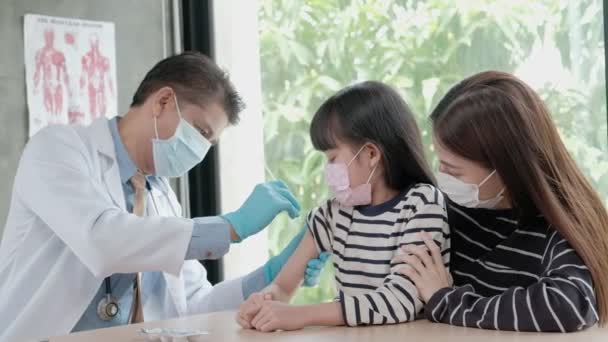 顔のマスクをした男性医師がアジアの女の子を予防するために予防接種 Covid 近くの母親と一緒に小児科病院で 注射は病気を治療し子供の痛みを引き起こす — ストック動画