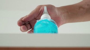 Düşük açı açısı ve beyaz arkaplanda yakın çekim: Adamın eli alkol jeli şişesine basınca aşağı doğru akmaya başlıyor. El yıkama Coronavirus (COVID-19) gibi hastalıkları ve bakterileri önler.).