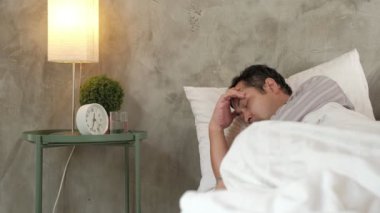 Asyalı ofis çalışanı işe gitmemiş, hastalık yüzünden geç kalkmış ve hastalık izni almış, ilaçlarını almış, evdeki kanepede beyaz battaniyelerle uyumuş, mendiller ve gri beton duvarın önündeki masanın üzerinde haplar varmış..