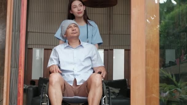 車椅子の高齢者は 家庭でリハビリテーションの治療を受け アジアの女性医師は 孤独を癒し 笑顔でそれらを奨励するために話すことによって治療を受けます — ストック動画