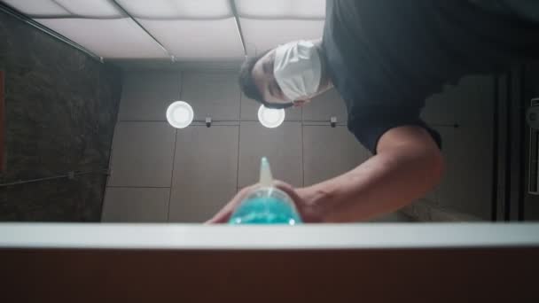 ロフトスタイルの天井の背景に撮影された低角度ビュー アルコールゲルドロップの顔マスクプレスボトルを持つ男と下に流れます 手洗いは病気を予防し コロナウイルスなどの細菌 Covid — ストック動画