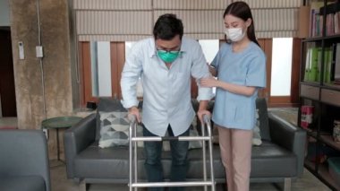 Asyalı bir kadın fizyoterapist engelli bir erkeğe evinde yürüteç kullanarak yardım ediyor, eğitiyor ve rehabilite ediyor. Fiziksel iyileşmeye rehberlik eden teşvik ve sağlık hizmetleri. 