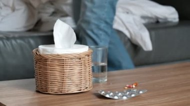 Illness Asian male worker absent from work and sick leave due to flu coughs and sneezes. Using tissue, taking medicines, sleeping under blankets on sofa in home.