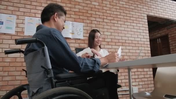 ビジネスオフィスの若い女性マネージャーは従業員にチャンスを与え 障害のある同僚はオレンジレンガの壁で会議室で働く機会を与えます 車椅子にいると怪我をする — ストック動画
