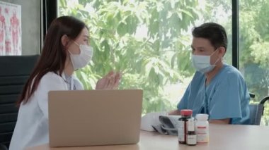 Tekerlekli sandalyedeki yaşlı engelli bir adamın sağlık, tıbbi terapi ve hastane kliniğinde rehabilitasyon sorunları hakkında yüz maskesi takan Asyalı kadın doktorlara danışmanlık yaparken yakın plan çekimleri..