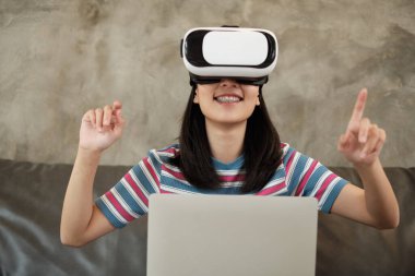 VR gözlüklü Asyalı kadın, 3 boyutlu sanal gerçeklik simülasyon oyunu izliyor. Etkileşimli eğlence teknolojisi aleti yenilikçidir. İnsanlar gelecekçi siber uzaya, modern yaşam tarzına giriyorlar..