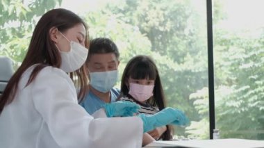 Koronavirüsü (COVID-19) önlemek için yüz maskeli kadın doktor Asyalı kızı aşılıyor. Çocuk hastanesindeki çocuk kliniğinde, babam yakınlardayken. Enjeksiyonlar hastalıkları tedavi eder, çocuklarda ağrıya neden olur..