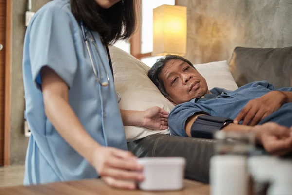 Female doctor checking the health of Asian elderly male patient at home as a medical service for visiting sick older people after retirement, medical support, residential caregiver from professional.