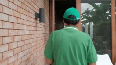 Yüzü maskeli yeşil üniformalı teslimatçı Asyalı kadının evine paket paketi veriyor. Çevrimiçi alışveriş, mobil uygulama üzerinden dijital ödemeler COVID-19 karantinasından yeni normal yaşam tarzı.