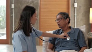 Kadın doktor, emekli olduktan sonra hasta yaşlıları, tıbbi desteği, profesyonel bakıcıları, hasta ziyaretleri için evde bulunan Asyalı yaşlı erkek hastanın sağlığını kontrol ediyor..