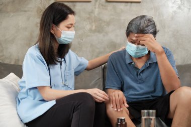 Yüz maskeli kadın doktor emekli olduktan sonra hasta yaşlıları ve profesyonel bakıcıları ziyaret etmek için evde bulunan Asyalı yaşlı erkek hastanın sağlığını kontrol ediyor.