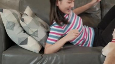 Güzel, sevimli, sıradan bir Asyalı kadın, oturma odasındaki gri kanepede mutlu bir şekilde oynayıp, takılıyor ve sevimli köpeğe (Fransız Bulldog) sarılıyor. Evcil hayvan onun ailesi ve yaşam tarzı..