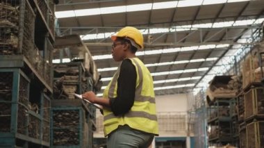 Güvenlik formları ve kasklarındaki siyah kadın işçiler endüstriyel fabrika deposundaki yedek motor parçaları ve makineleri kontrol ediyor. Ve neşeli beyaz erkek mühendis meslektaşı tarafından karşılandı..