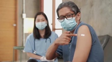 Yüz maskesi takmış yaşlı bir erkek hasta ve aşı sonrası baş parmak uçlarında Asyalı bir kadın doktor. Bu bir huzurevi sağlık hizmeti. Grip virüsünü, ateşi ve sağlıklıyı önlüyor.. 