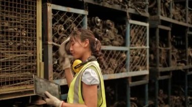 Güvenlik üniformalı Asyalı kadın işçi kasklarını çıkardı, endüstriyel fabrikalardaki yedek motor ve makine parçaları deposundaki yorgunluktan dolayı terini silmek için kolunu kaldırdı..