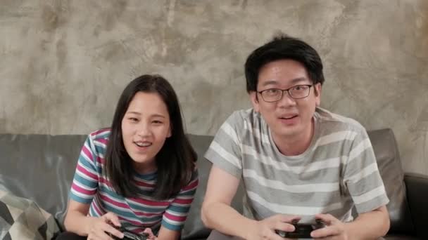 亚洲男人很喜欢和他的女朋友玩电子游戏 坐在客厅的沙发上 用操纵杆控制比赛 家庭娱乐技术是一种家庭生活方式 — 图库视频影像