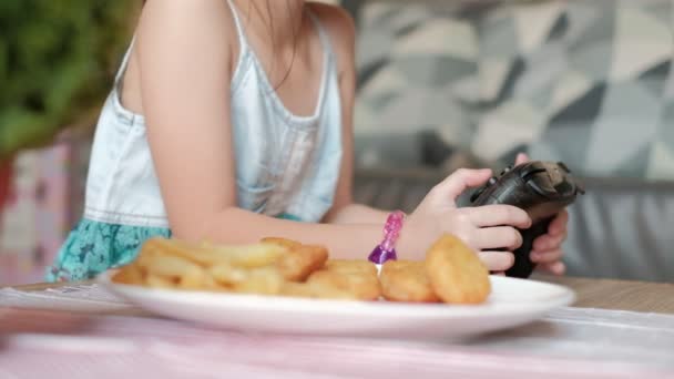 クローズアップVdoは 子供の手を示して Joystickがビデオゲームをプレイし ファーストフード フランスのフライドポテト ナゲット ケチャップで白い料理を食べることを強制します オンラインエンターテイメント技術は子供を中毒にする — ストック動画
