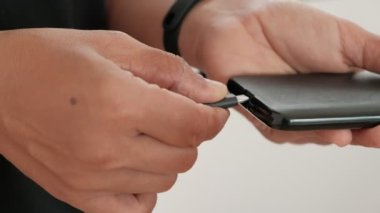 Ön yakın çekim: Güç USB kablosunu siyah bir cep telefonunun arka portuna bir adamın kolunu kullanarak şarj etmek. Beyaz arkaplanda bir hat oluşturun. Aygıtlar dijital teknolojide kullanılır.