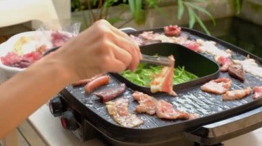 Yakın plan, kadının elleri yemek pişiriyor, domuz eti, mürekkep balığı ve pastırma dilimleri gibi taze et büfeleri pişiriyor. Barbekü ya da Shabu mutfağı piknik ve öğle yemeği partileri için lezzetli bir yemektir..