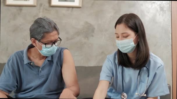 アジアの女性医師は ウイルス感染から病気を防ぐためにマスクをしている高齢者をワクチン接種しています 引退した病人を治療するのは専門家による在宅医療です — ストック動画