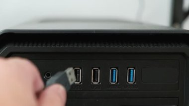 Ön taraftaki yakın çekim görüntülerinde USB kablosu siyah masaüstü bilgisayarına beyaz arkaplan önünde bağlanıyor. Yanda güç düğmesi ve hoparlör var..