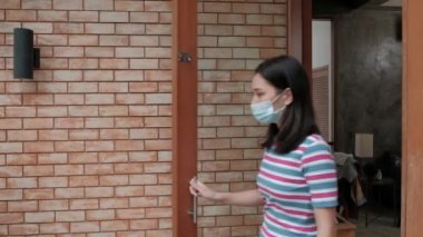 Yüzü maskeli yeşil üniformalı teslimatçı Asyalı kadının evine paket paketi veriyor. Çevrimiçi alışveriş, mobil uygulama üzerinden dijital ödemeler COVID-19 karantinasından yeni normal yaşam tarzı.