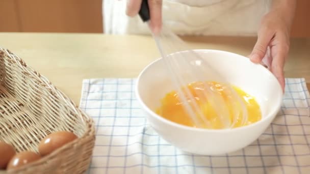 エプロンの女性料理人は 家庭の台所の木製のテーブルの上に白いボウルに有機卵を泡立てて 食品成分と混合し 自家製パン屋のために焼く 新鮮な黄身 栄養健康的な朝食 — ストック動画