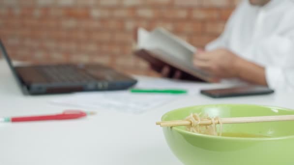 Asian Male Worker Reads Appointment Book While Eating Instant Noodles — Stock Video