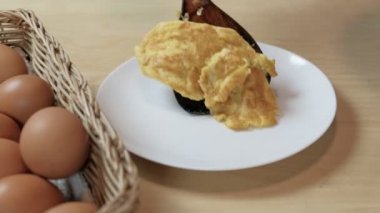 Şef omleti, spatula kullanarak, ev mutfağındaki ahşap masadaki boş beyaz tabakta kepçelendi. Kızarmış yumurta sarısı yüksek protein, kalori ve lezzetli sağlıklı yemektir ama daha fazla kolesteroldür.. 