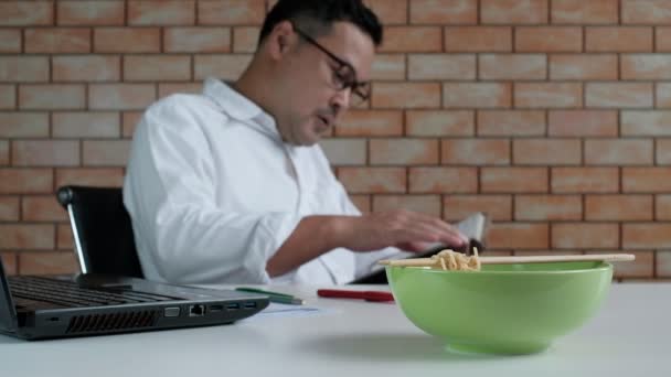 Asian Male Worker Reads Appointment Book While Eating Instant Noodles — Stock Video