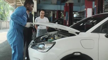 Kadın müşteri ve Asyalı erkek müdür, siyah tamirci kadın, EV motor tamiratı ve pil garantisi, otomotiv garajında müşteri hizmetleri bakımı ve ulaşım endüstrisi konularını görüştü..