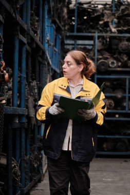 Bir İspanyol yetişkin kadın müfettiş otomatik makine yedek parça stoklarını kontrol ediyor. Depodaki stoklar, dağıtım fabrika işletmeleri, endüstriyel işçiler ve operatör işleri..