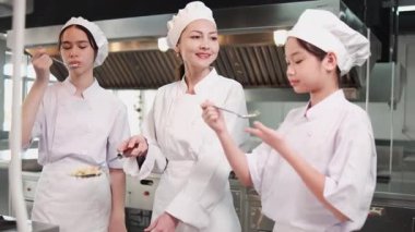 Beyaz kadın usta şef, stajyer öğrenci kızları eğitir, tavada lezzetli pilav pişirir ve restoran mutfağında lezzet tatma, lezzetli yemeklerde profesyonel gurme ve aşçılık yemekleri yapar..