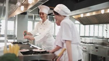 Kadın şef stajyer öğrencilere, yemek pişirme kursuna, yemek pişirme mutfağında profesyonel gurme ustasına lezzetli yemekler pişirmede malzeme hazırlama ve aşçı yemeklerine gösteri yapıyor..