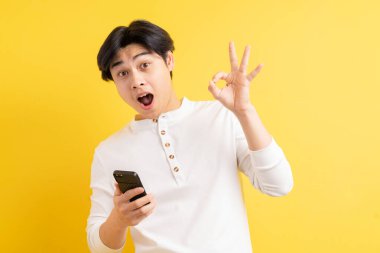 Asyalı adam şaşırmış bir suratla telefonunu kullanıyor.