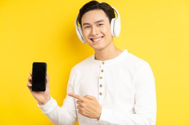 Asyalı işadamı müzik dinlemek için kablosuz kulaklık takıyordu ve parmağı elinde tuttuğu cep telefonunu gösteriyordu.