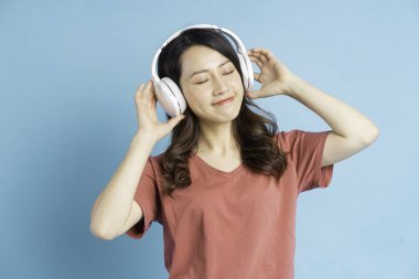 Güzel Asyalı kadın, beyaz kablosuz kulaklık takıyor ve elinde telefonla müzik eşliğinde dans ediyor.