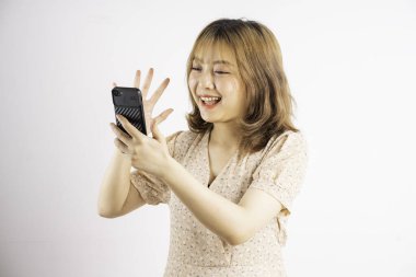 Asyalı genç bir kız telefonu elinde tutuyor. İfadeleri ve jestleri var.