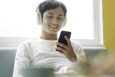 Asyalı adam oturuyor, müzikten hoşlanıyor.